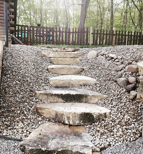 Wide stone slab steps set into a gravel bank beside a wooden fence, with rock either side holding the grade.